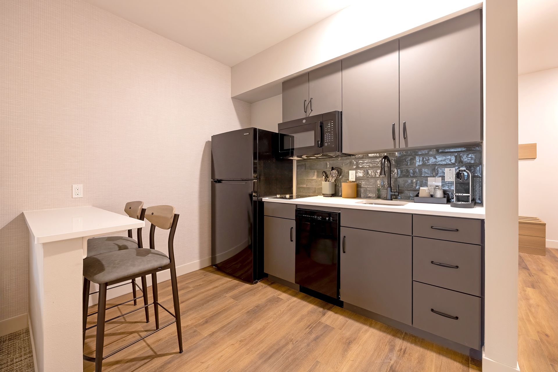 Kitchen with gray cabinets, black appliances, a counter-height table, and two stools.