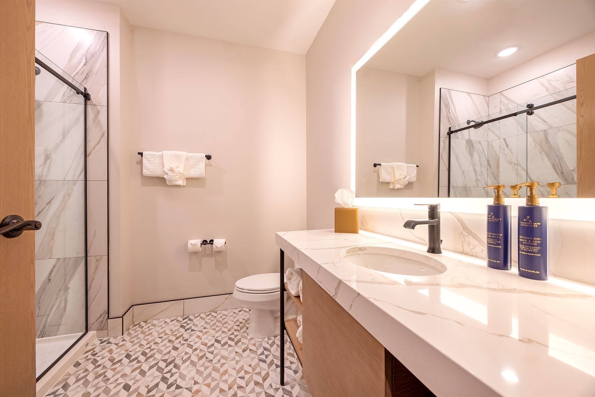 Modern bathroom with marble countertops, stone tile floor, glass shower, and large mirror.