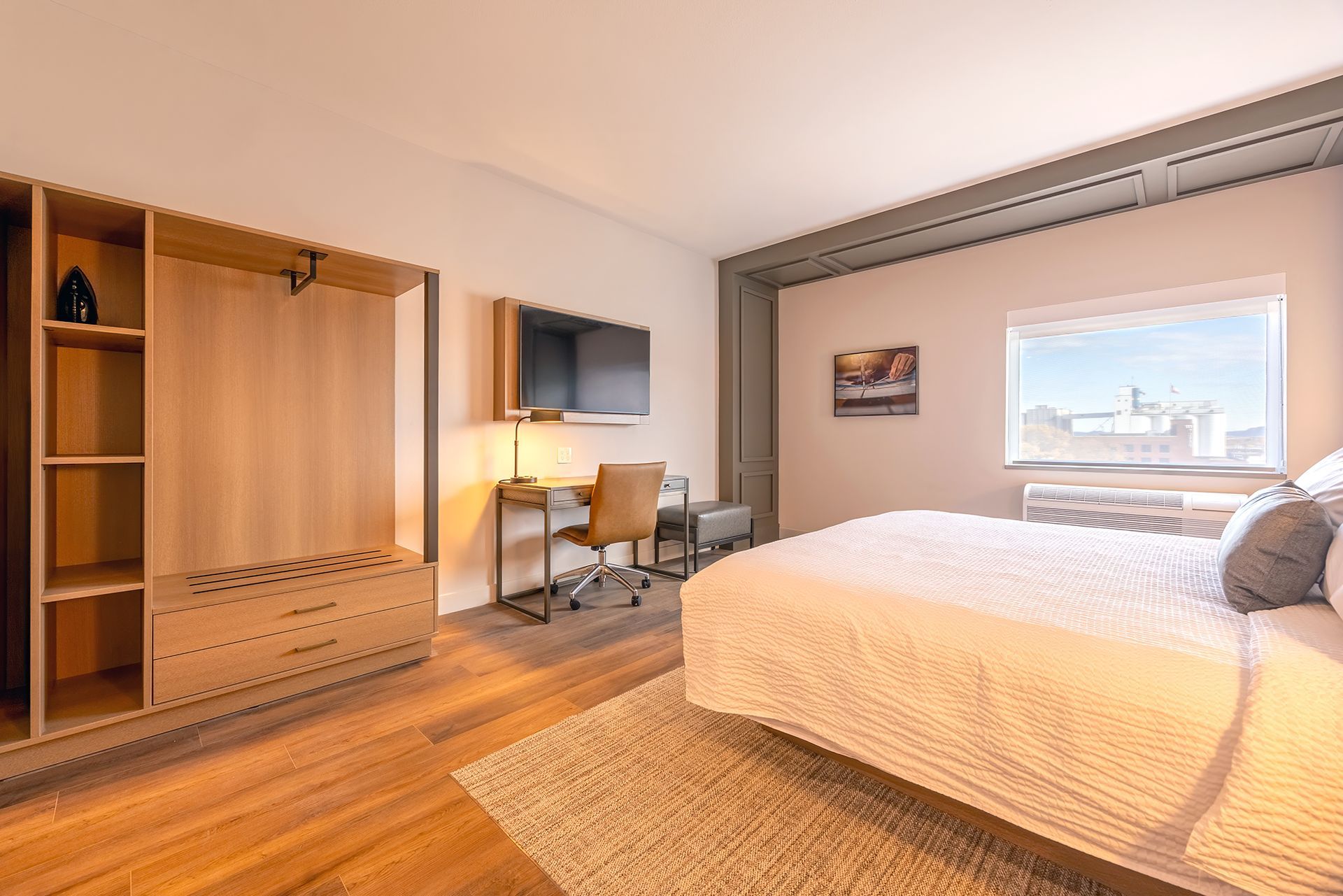 Modern hotel room with a bed, desk, wardrobe, and window overlooking a city.