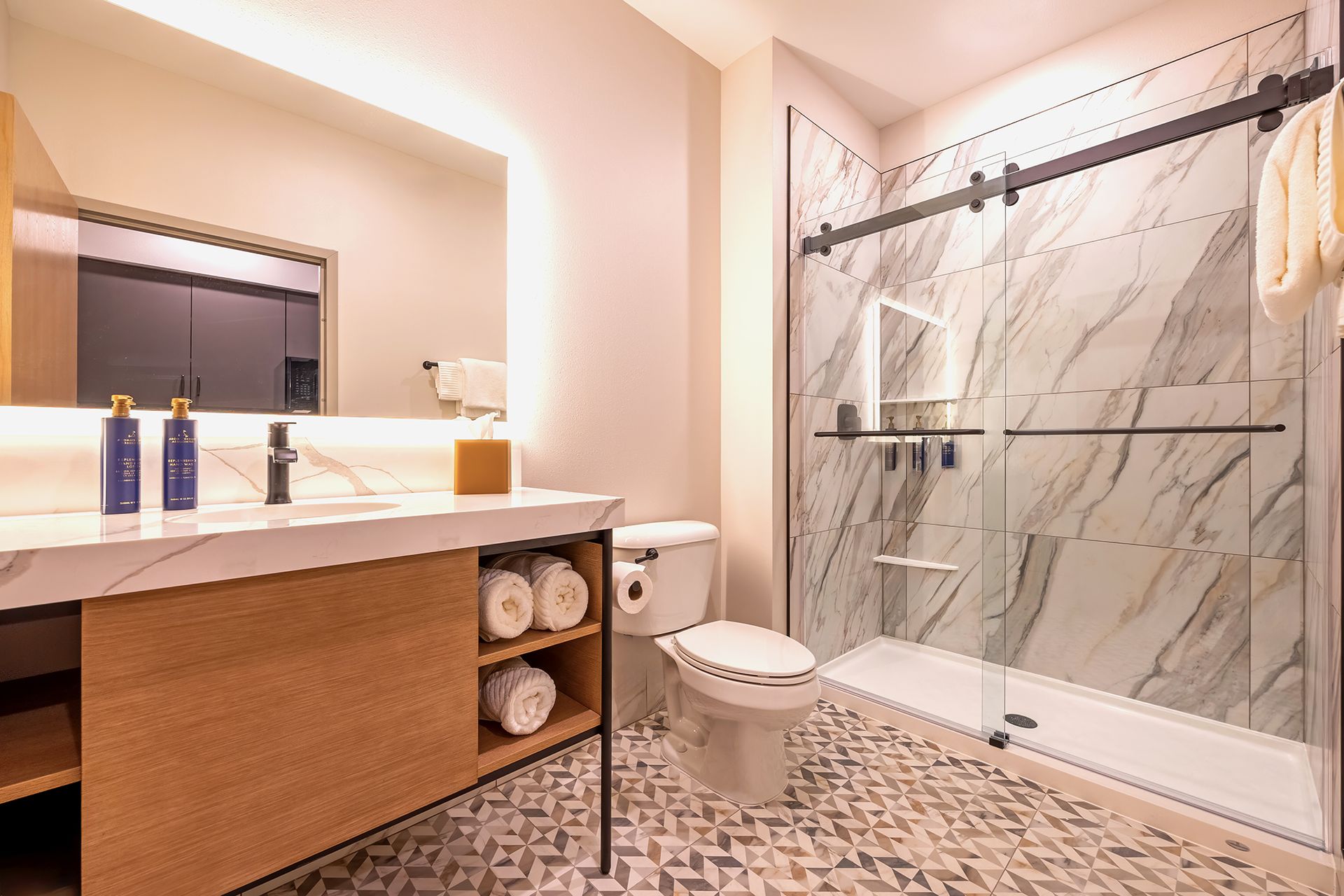Modern bathroom with marble shower, vanity with gold accents, and patterned tile floor.