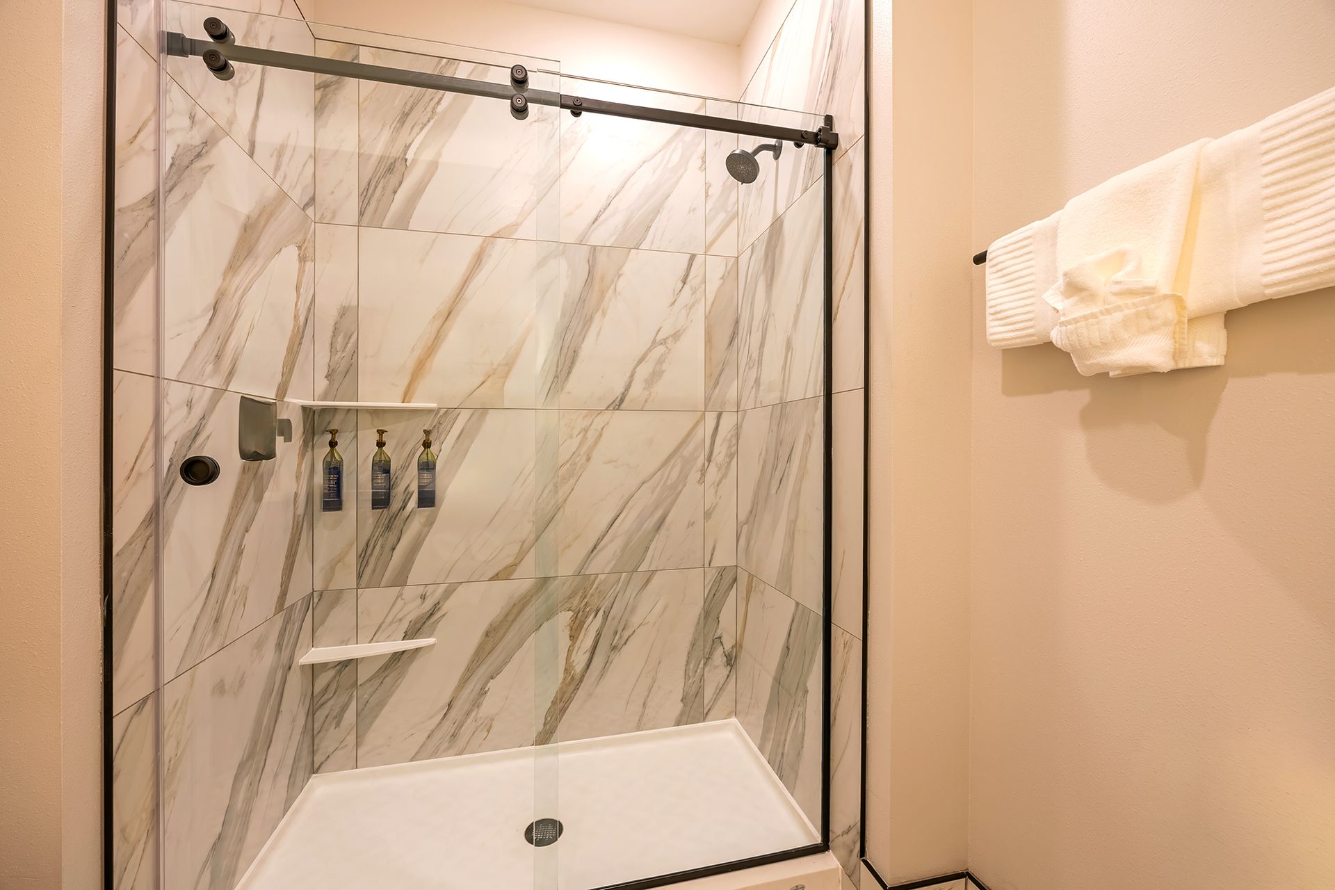 Bathroom with marble-patterned tile, glass shower door, and a white towel on a wall-mounted rack.