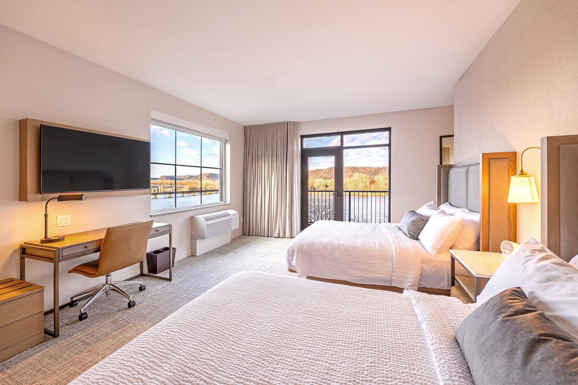 Modern hotel room with two queen beds, a desk, a television, and a balcony with a view.