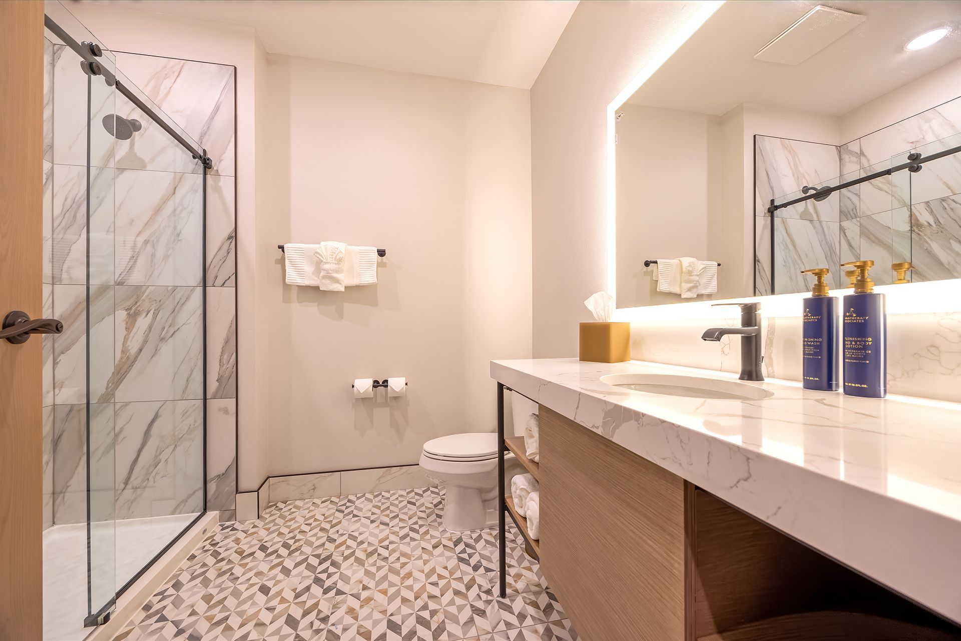 Modern bathroom with marble shower, sink, toilet, and patterned tile floor.