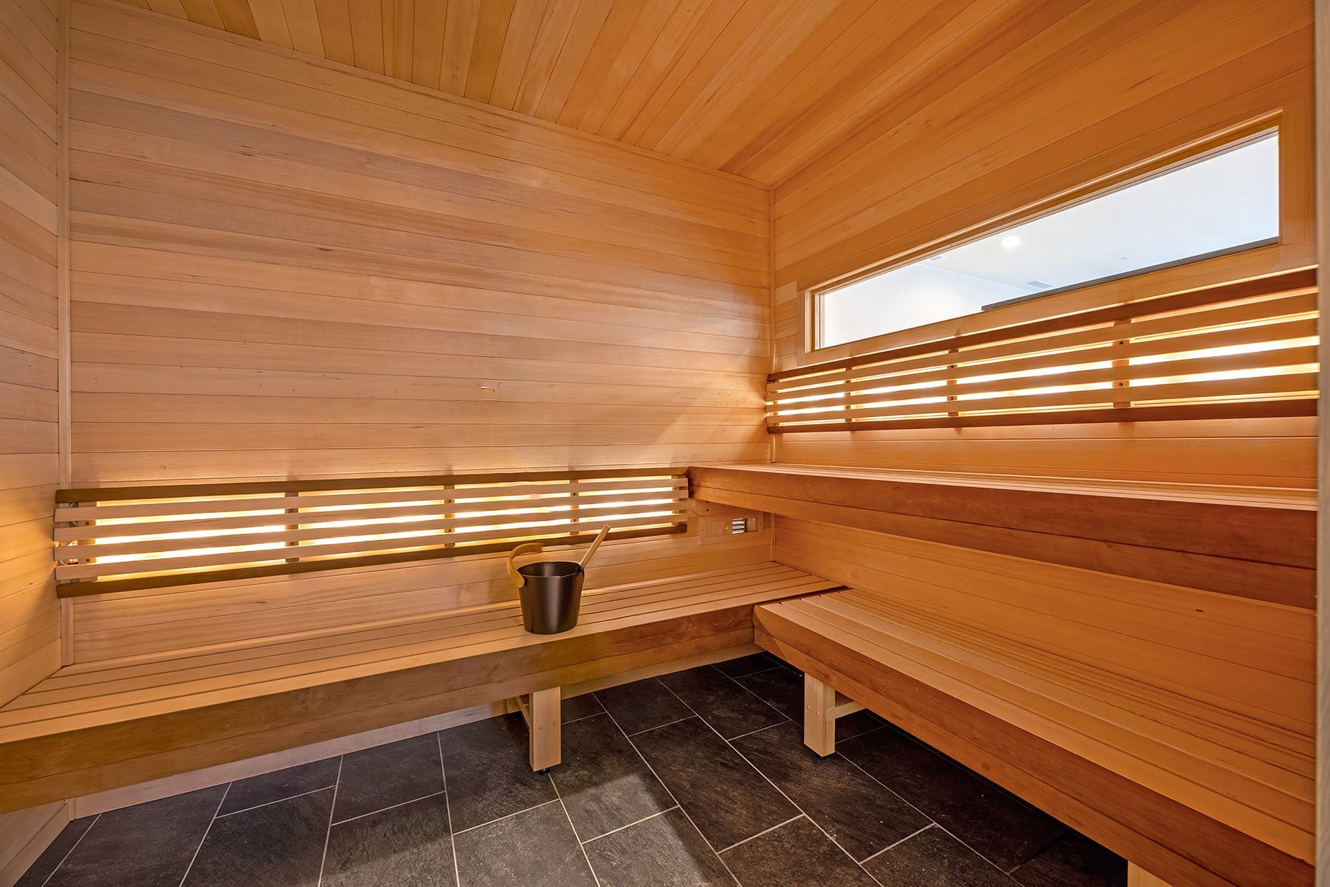 Wooden sauna interior with benches, bucket, and small window.