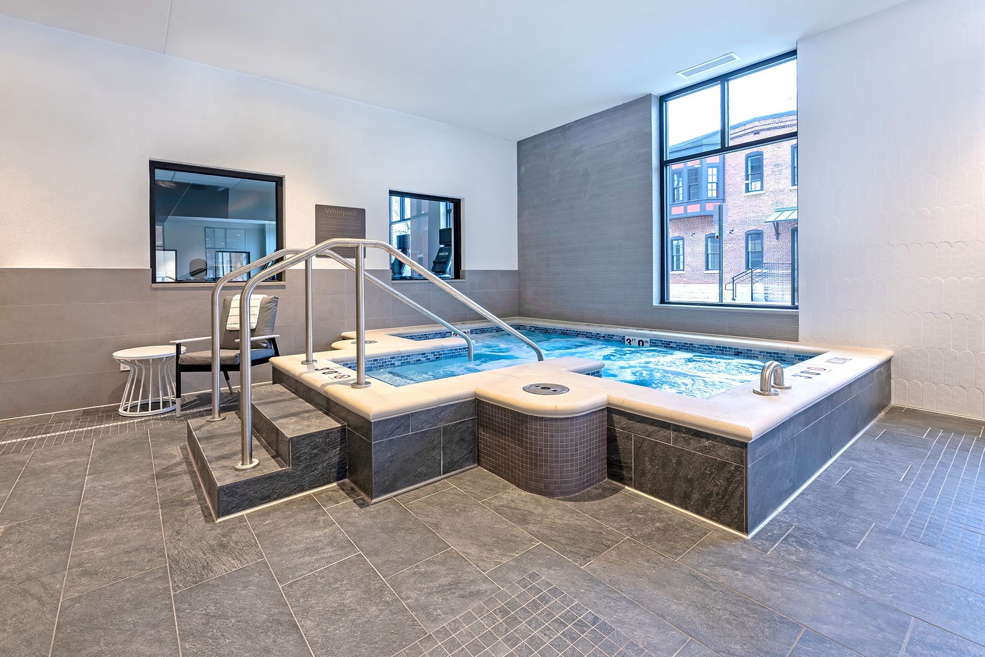 Indoor jacuzzi with handrail and steps, next to a window and wall mirrors.