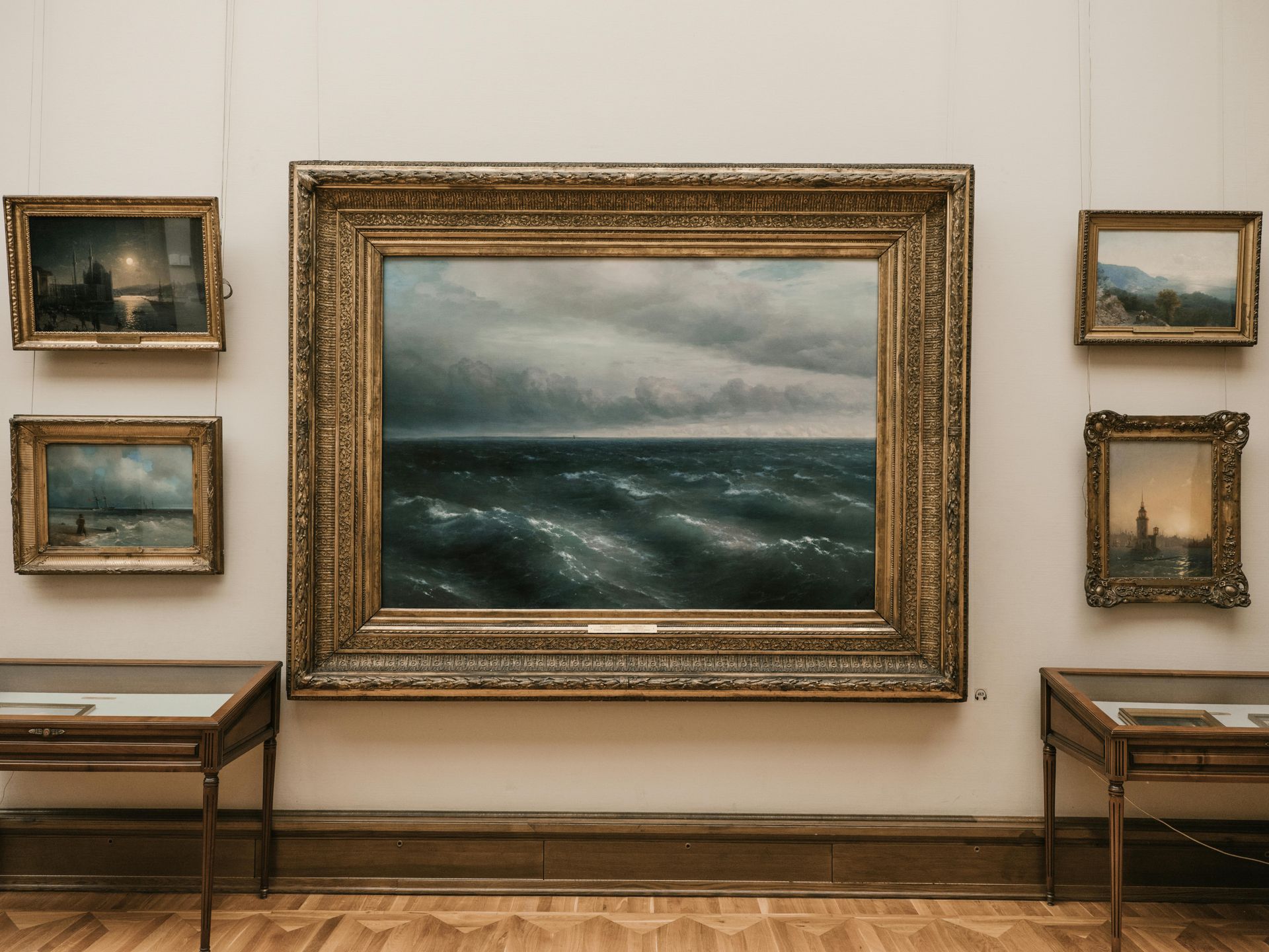 Artwork display in a gallery with a large seascape painting as the focal point, surrounded by other framed works. MMAM- Minnesota Marine Art Museum