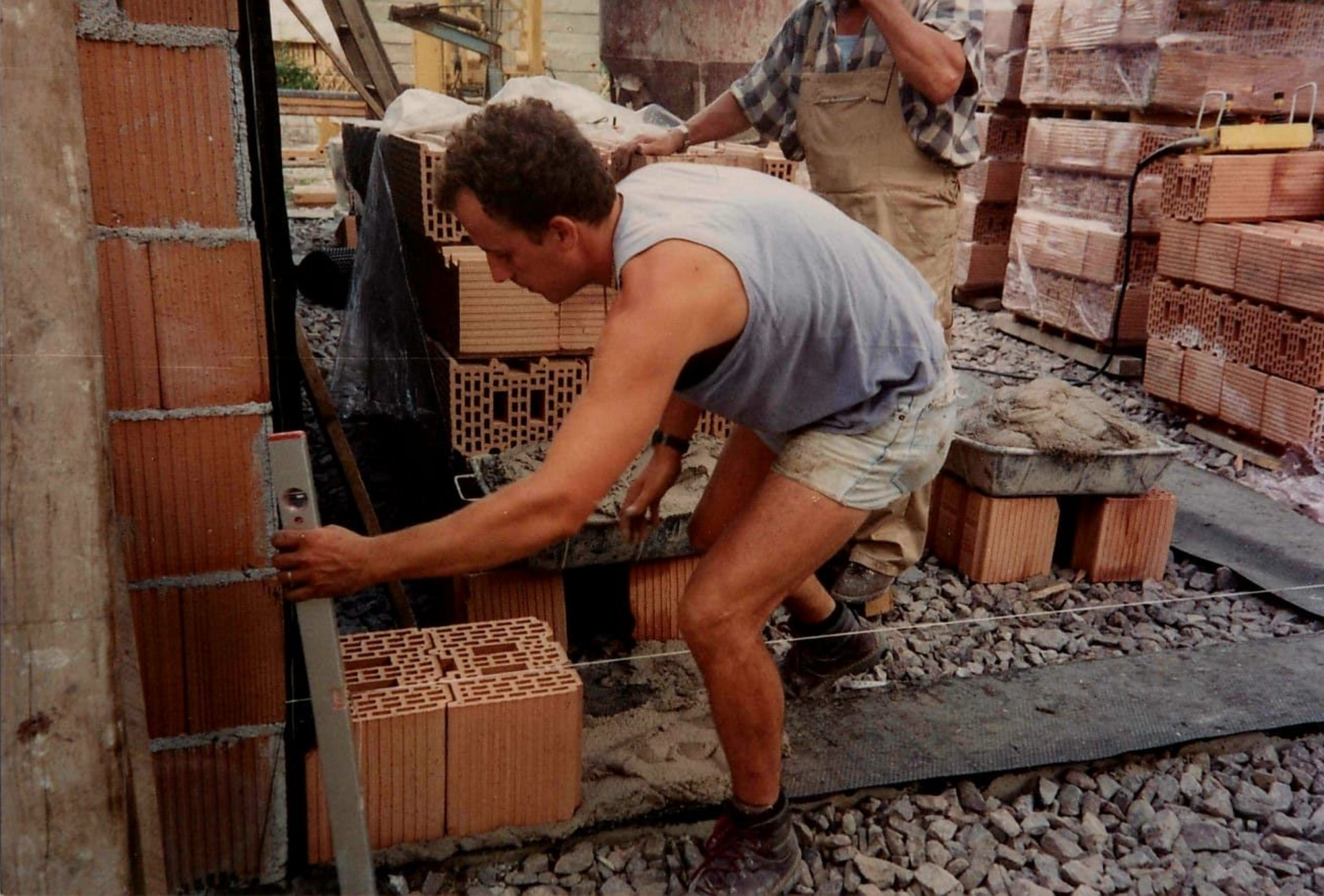 Uomo che usa la livella per costruire un muro di mattoni in un cantiere edile.