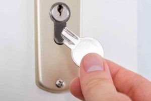 A person is holding a key in front of a door lock.