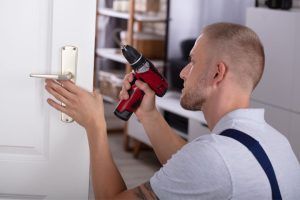 A man is fixing a door handle with a drill.