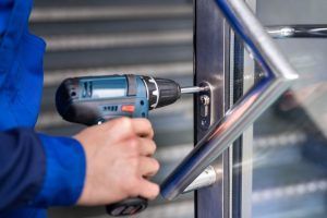 A man is using a drill to fix a door handle.