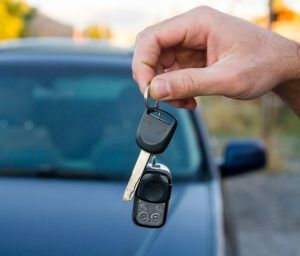 A person is holding a car key in front of a car.