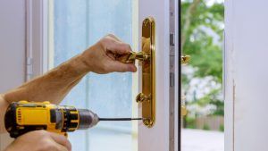 A man is using a drill to fix a door handle.