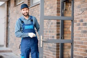 A man in blue overalls is standing in front of a door.