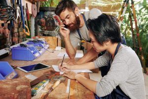 A man is talking on a cell phone while a woman writes on a piece of paper.