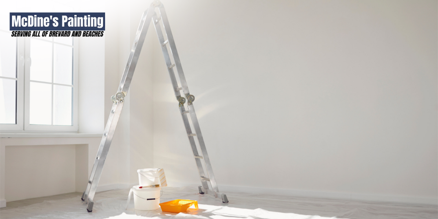 An empty room with a ladder and a bucket of paint.