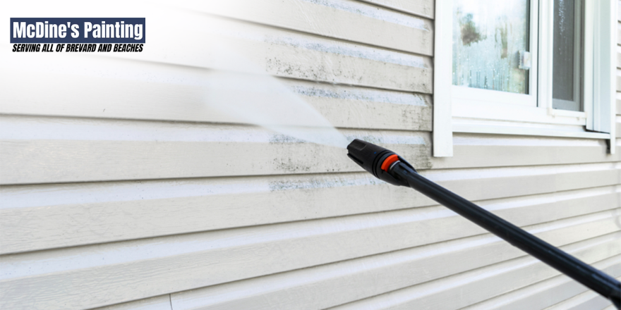 A person is cleaning the side of a house with a high pressure washer.