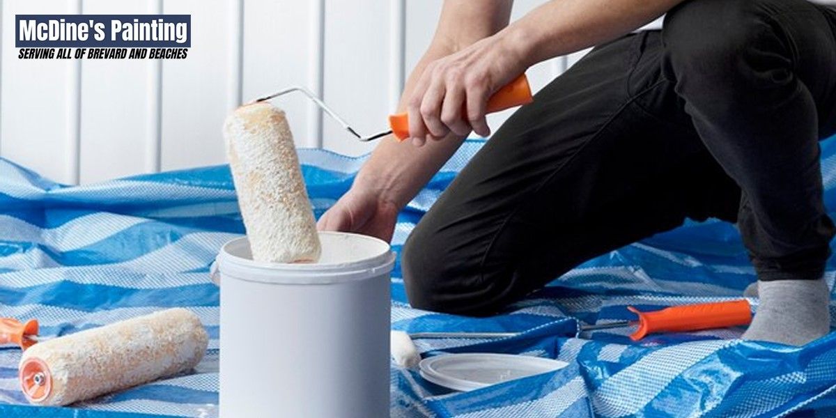 A man is kneeling down while holding a paint roller.