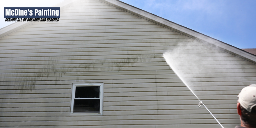 A man is using a high pressure washer to clean the side of a house