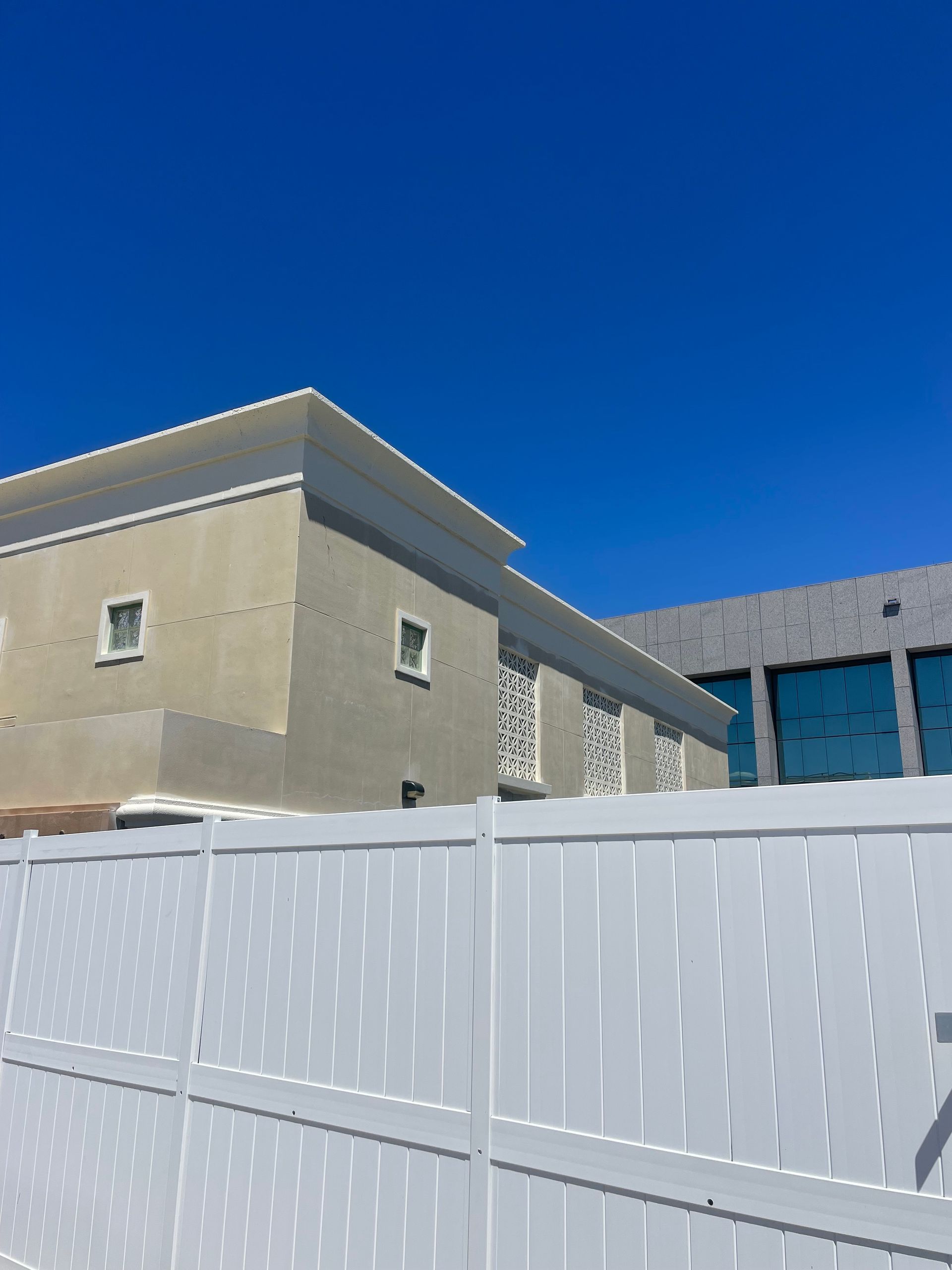 A white fence surrounds a building with a blue sky in the background