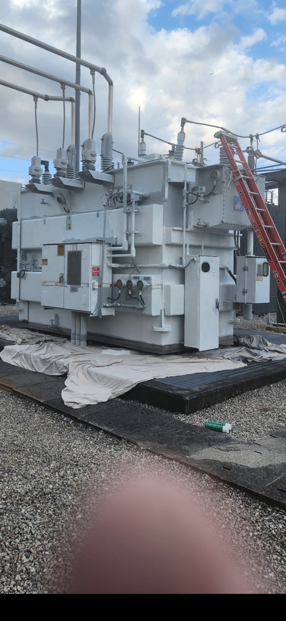 A large white transformer is sitting on top of a gravel lot.