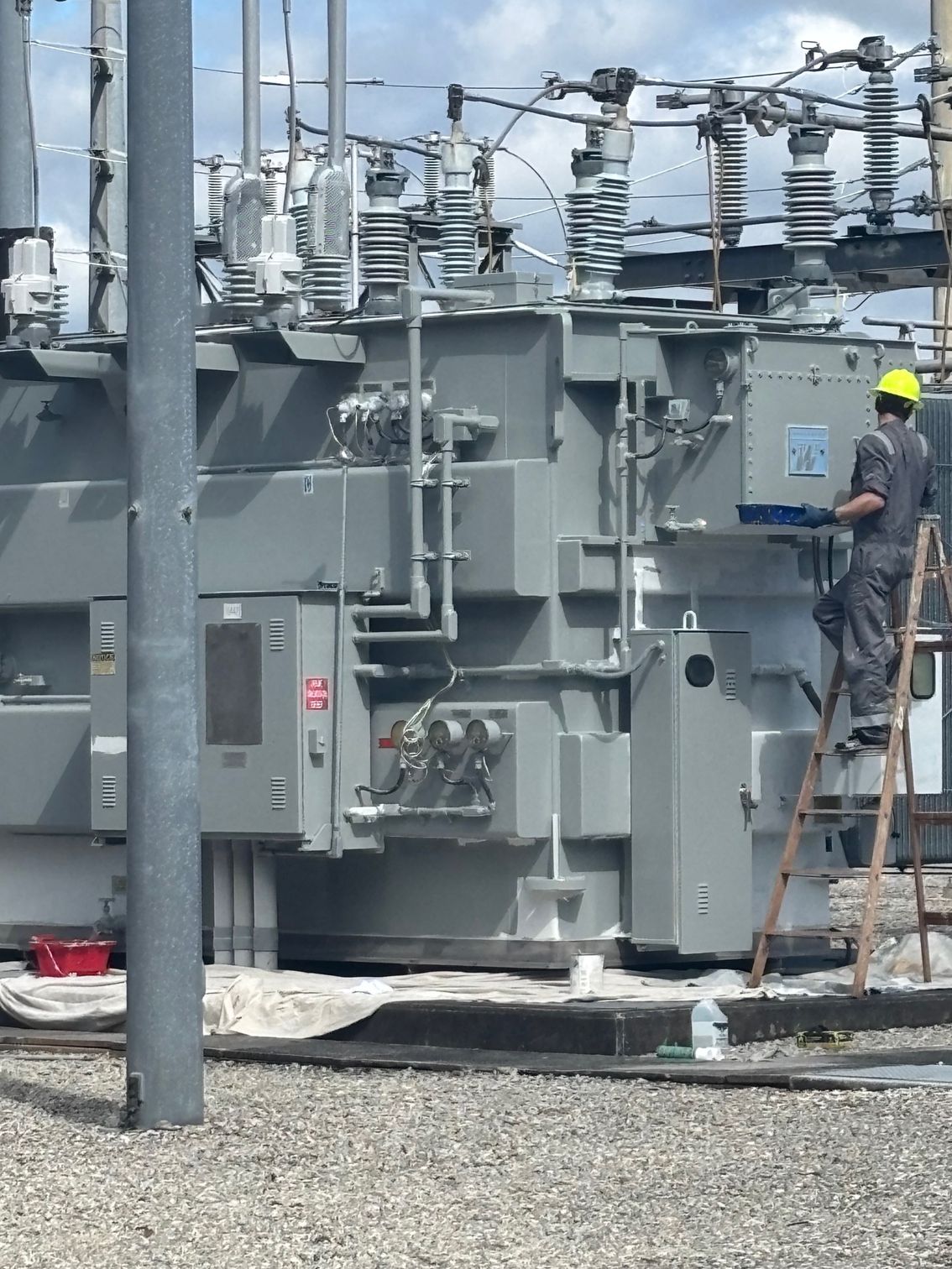 A man on a ladder is working on a large transformer