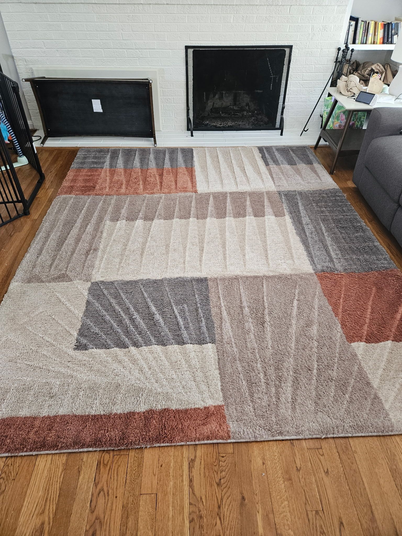 A rectangular patterned rug with blocks of beige, rust, and gray, in front of a fireplace.