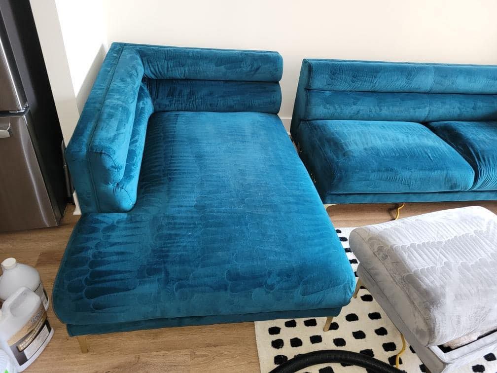 Teal chaise lounge and sofa in a room, with a rug and cleaning supplies.