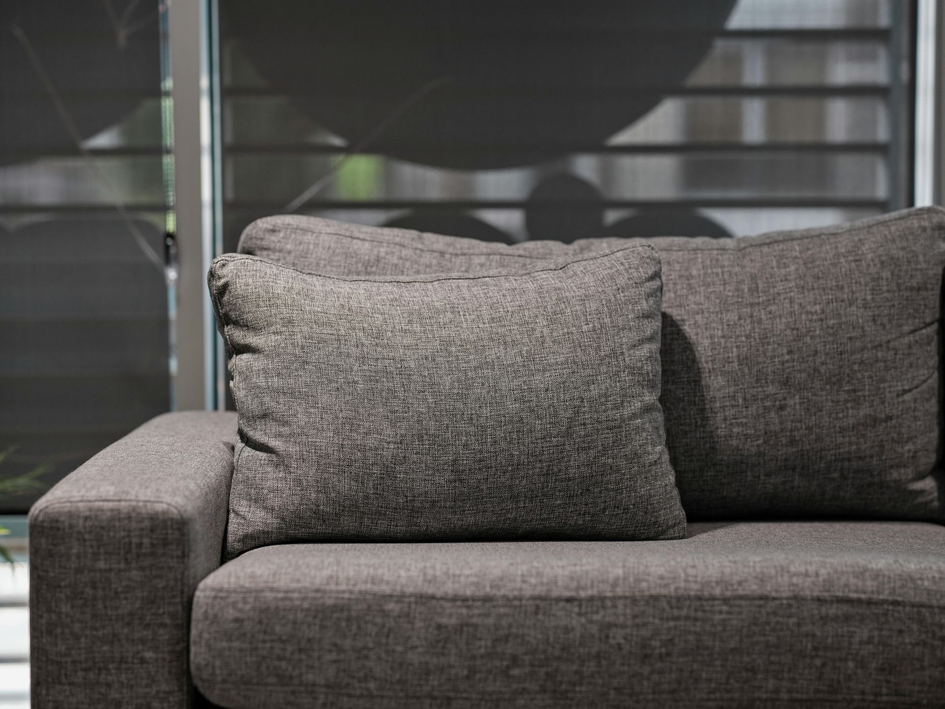Gray couch with two matching pillows, near a window with blinds.