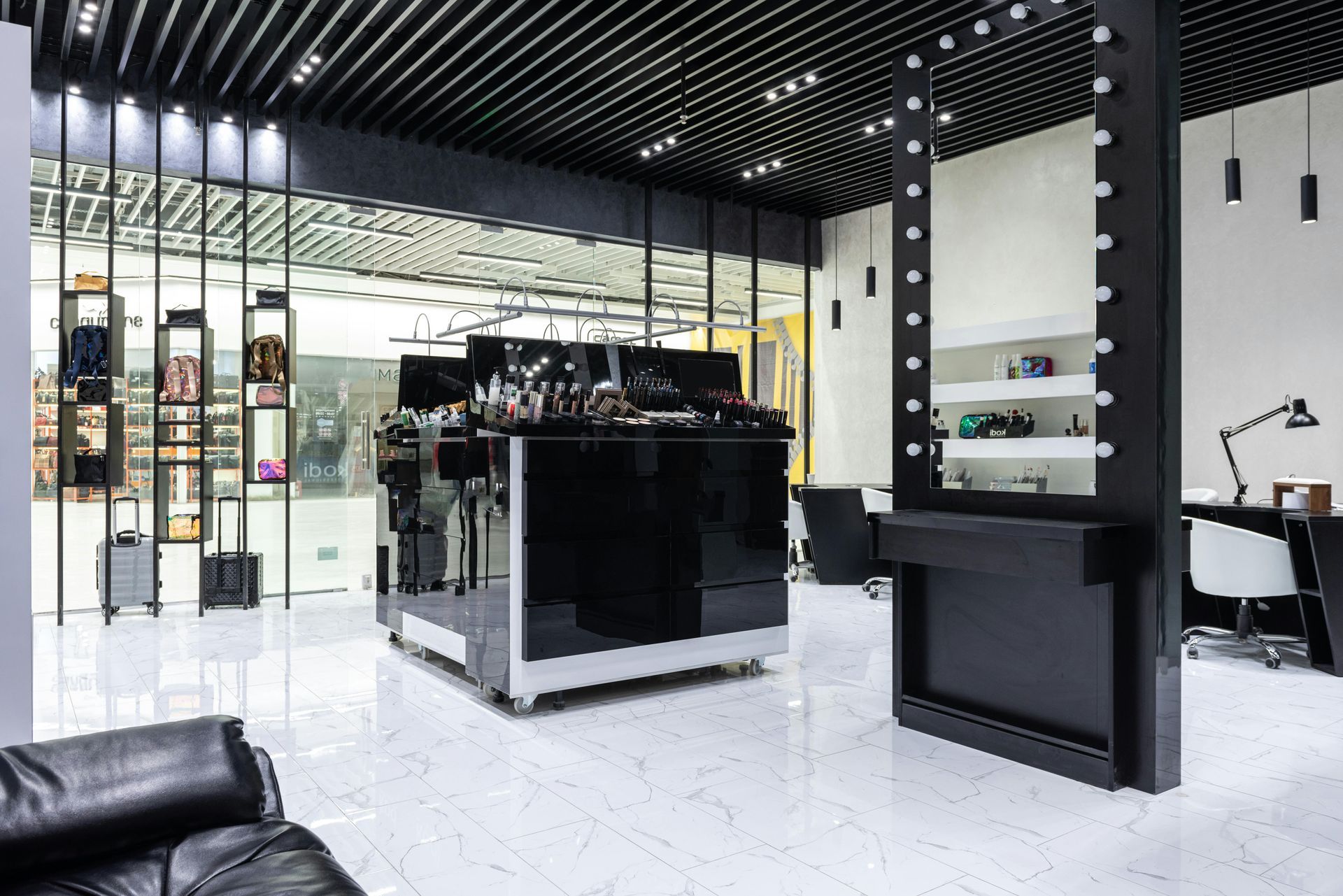 A modern black and white makeup studio interior with shelves and a large mirror.