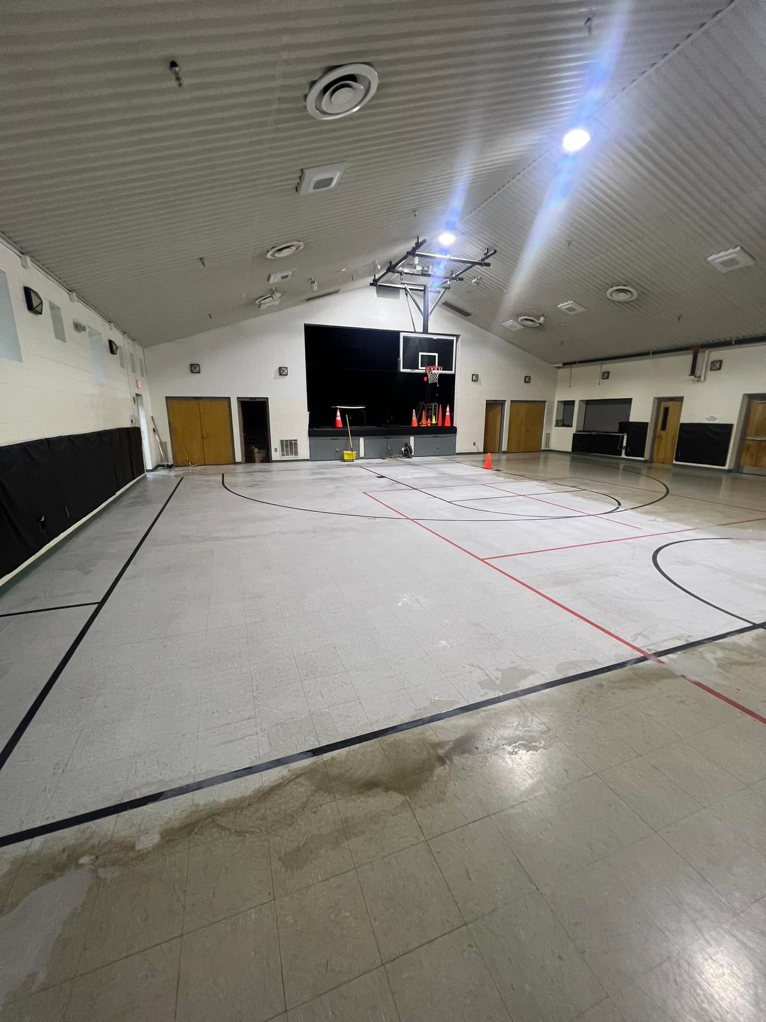 An indoor basketball court with lines and a hoop.  The floor is wet in spots and the walls are white.