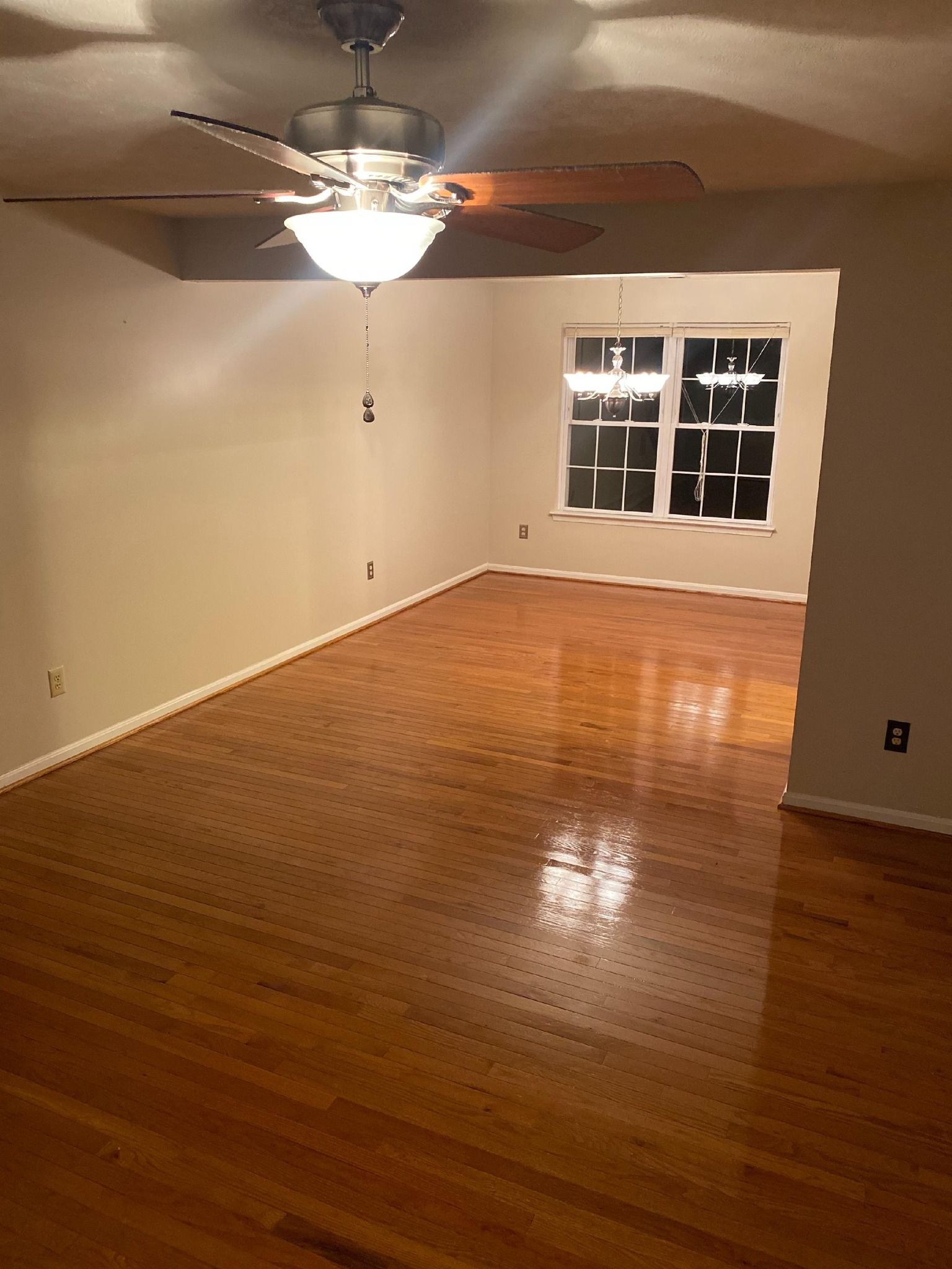 Wooden floor, light walls, ceiling fan with light, window, and light. Empty room.