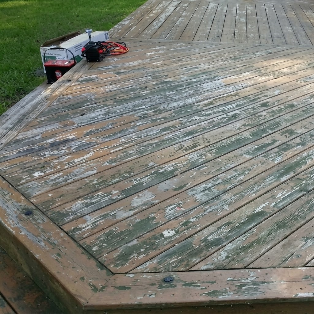 Weathered wooden deck with railings, surrounded by green trees and sunlight.