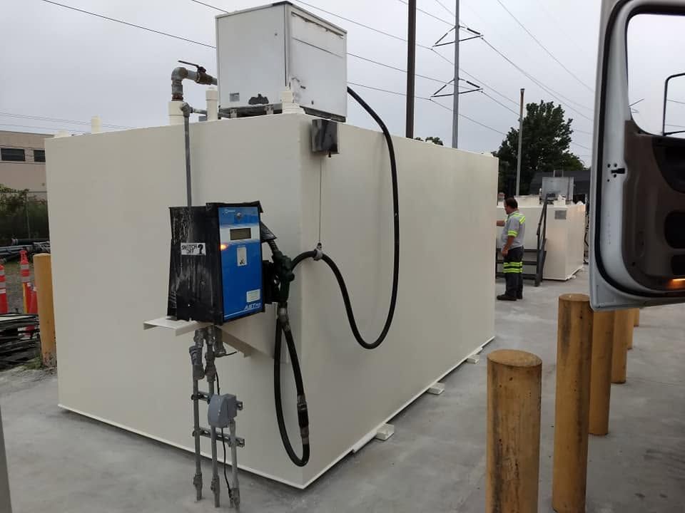 White industrial equipment enclosure with attached blue pump and hoses outdoors on pavement