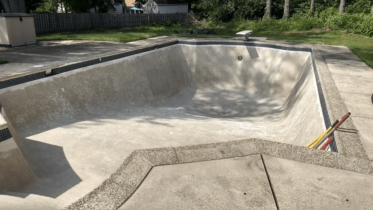 Empty concrete swimming pool with sloped sides and a small section of multicolored hoses at the edge