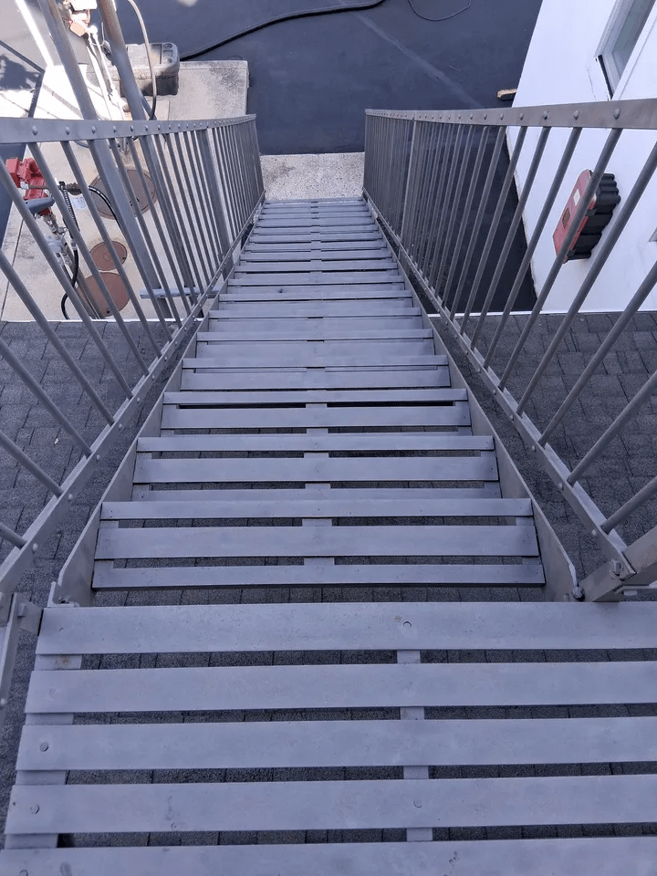Stairway with gray metal steps and railings leading down to a paved landing above water