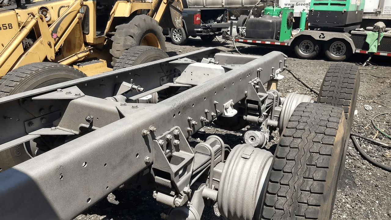 Damaged truck chassis and wheels in a scrapyard, with heavy equipment in the background