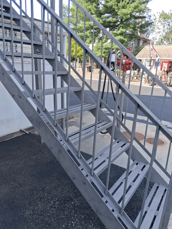 Gray metal outdoor staircase beside a building, with railings and steps leading up to an upper level