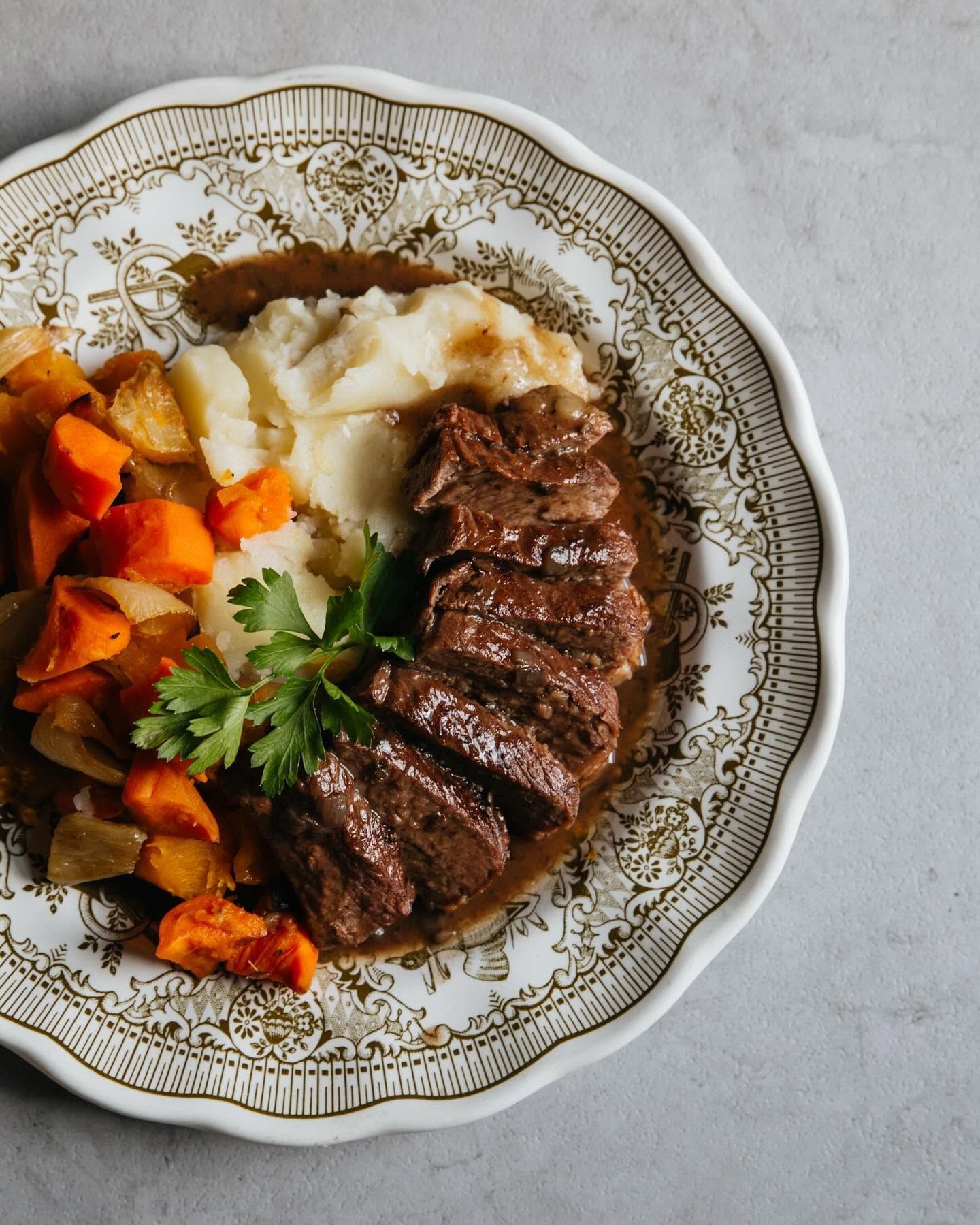 Plated steak with mashed potatoes and roasted vegetables on an ornate white plate