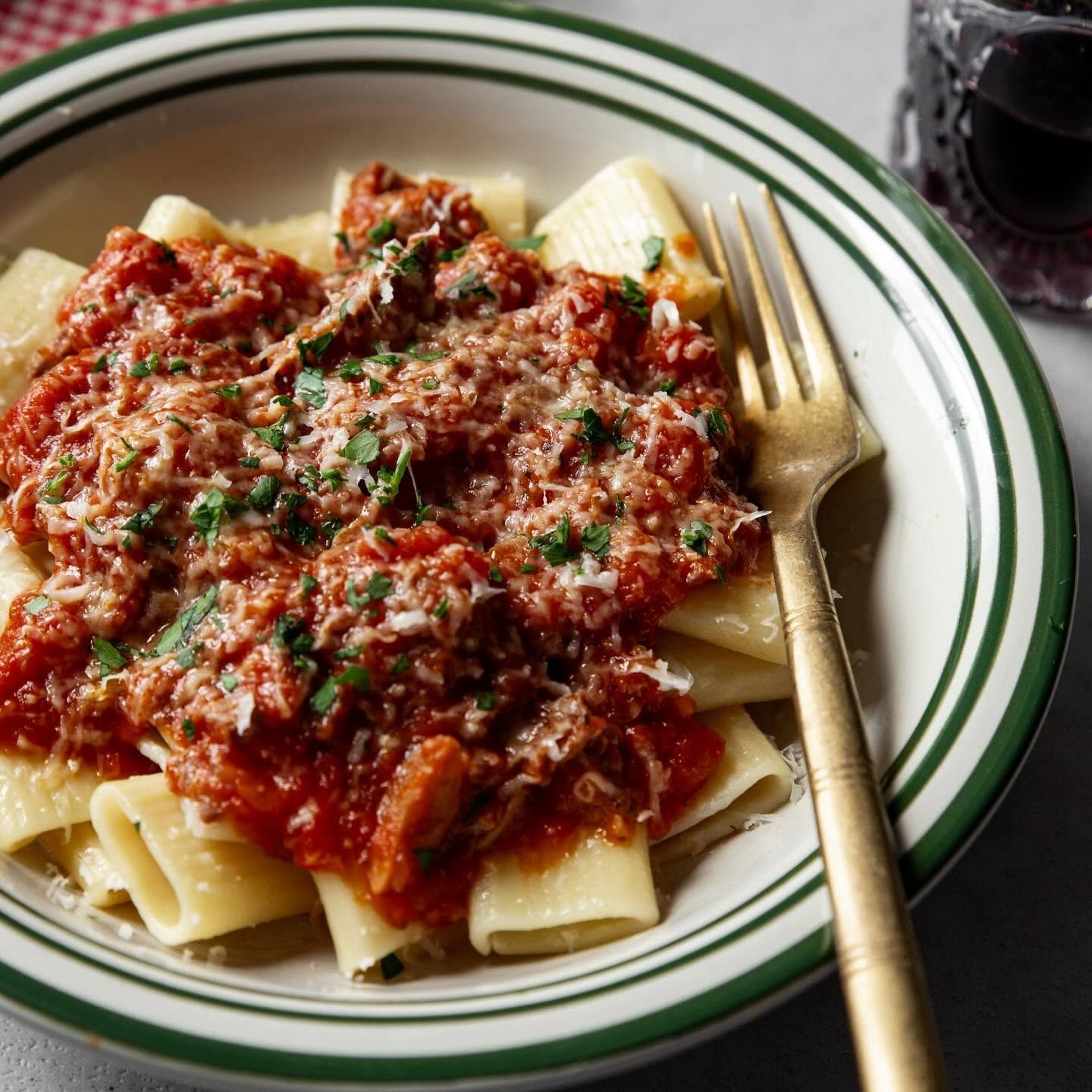 Plate of rigatoni with red meat sauce and grated cheese, garnished with parsley, beside a fork