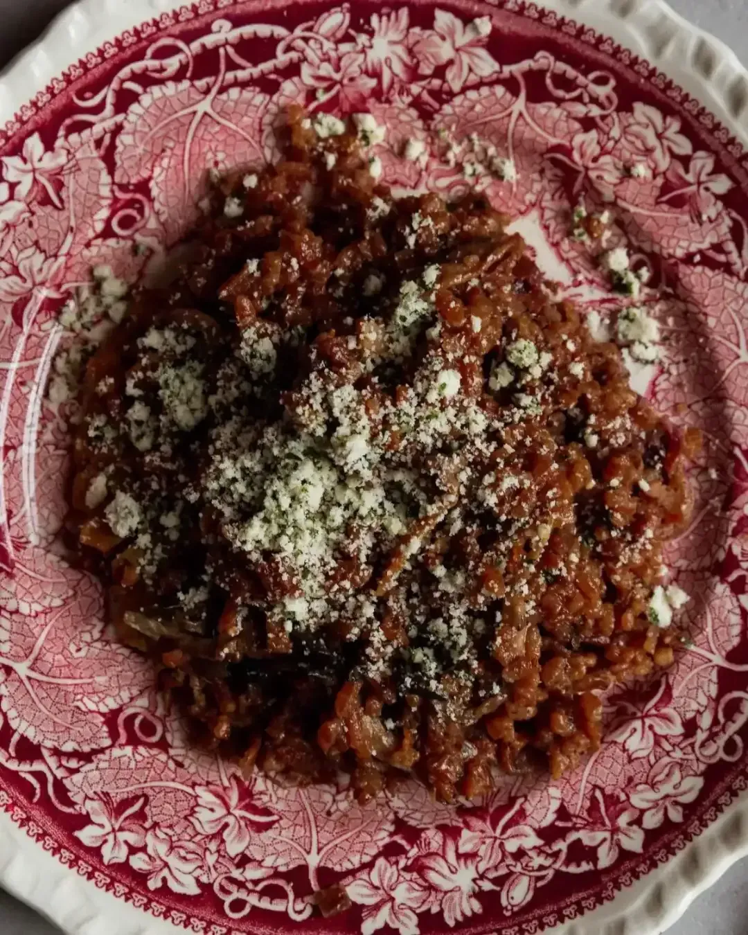 Red pasta on a pink patterned plate, topped with grated cheese.