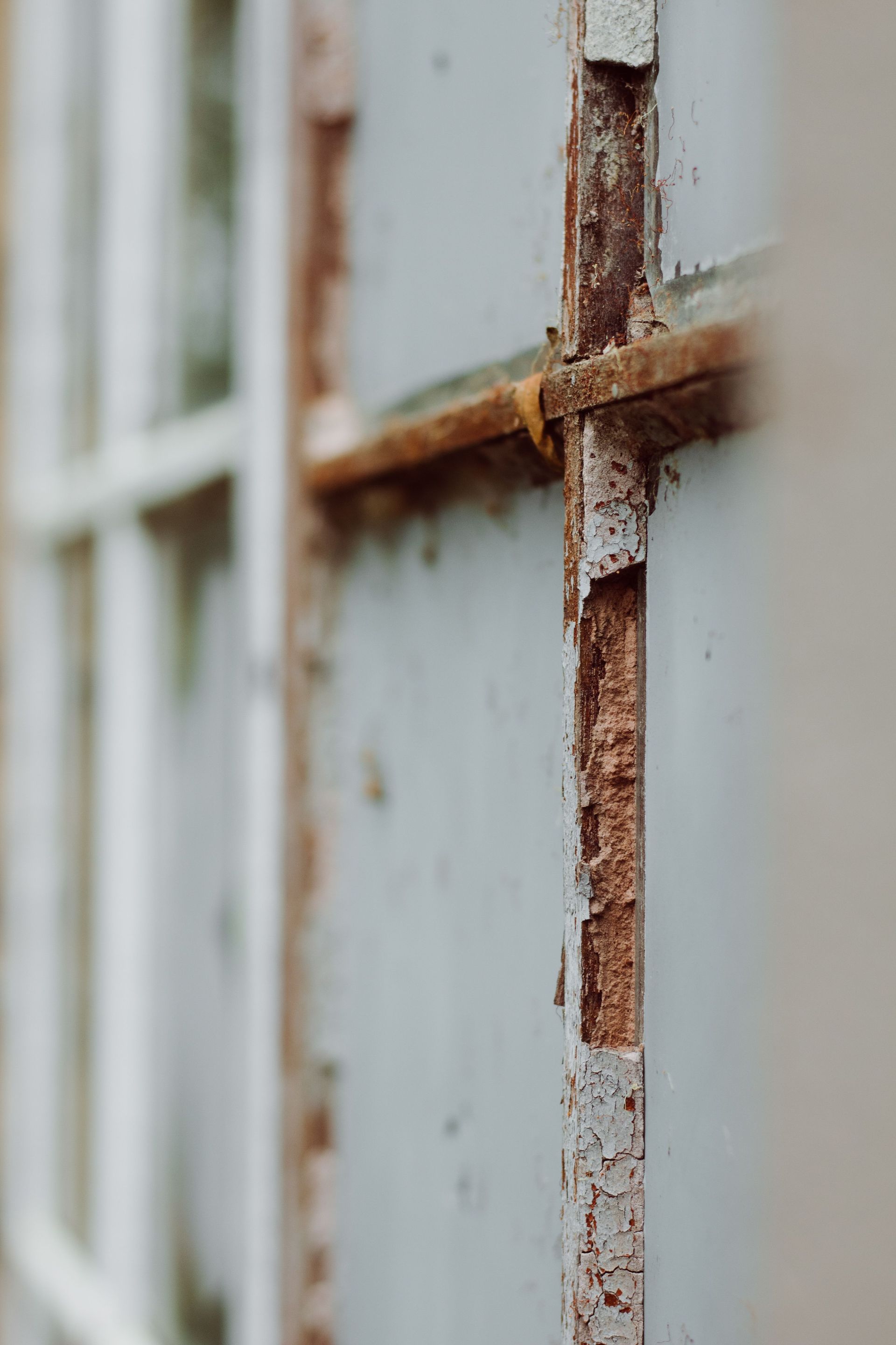 Close-up of a rusty window frame with peeling white paint and blurred panes in the background