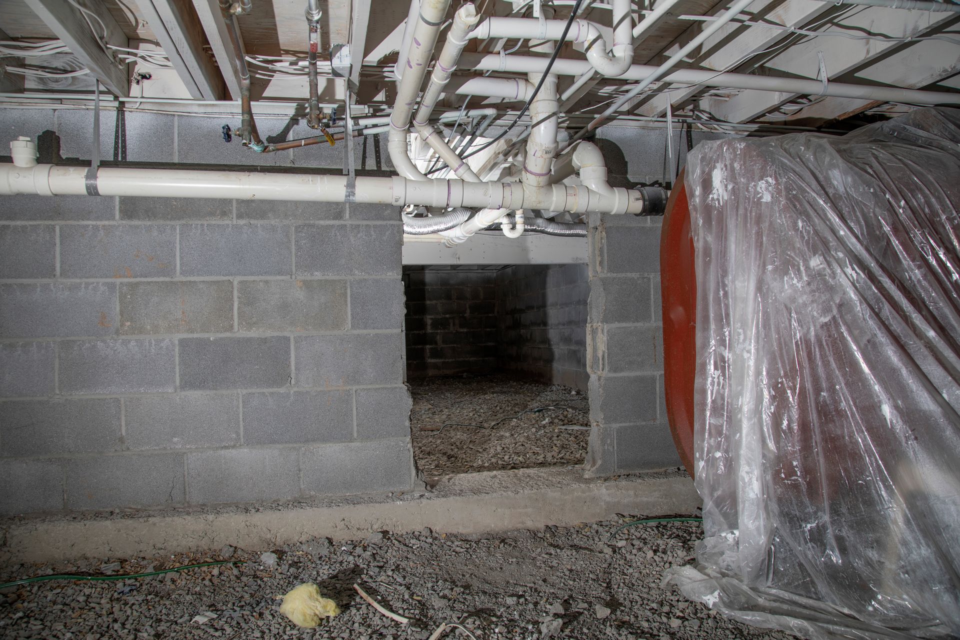 crawl space encapsulation near me Basement interior with concrete block walls, pipes, and a large tank covered in plastic.