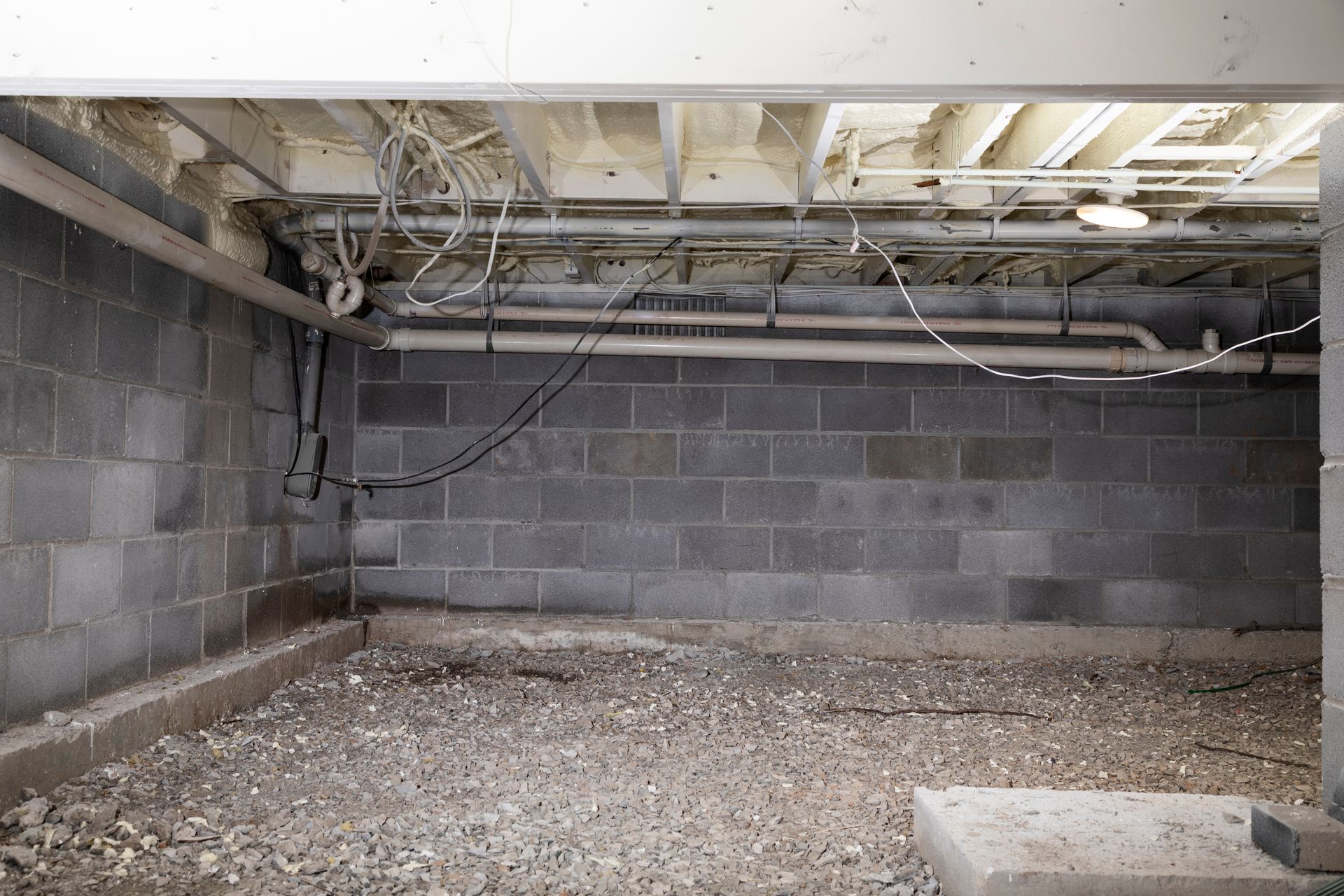 crawl space encapsulation buford ga Interior view of a basement with concrete block walls, exposed pipes, and gravel floor.