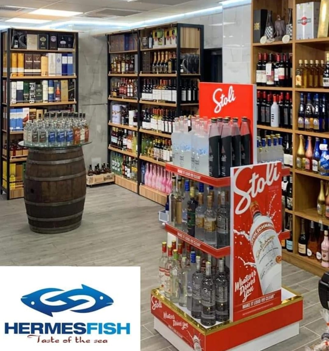 Liquor store aisle with shelves of bottles and a red Stoli vodka display stand; Hermesfish logo in corner