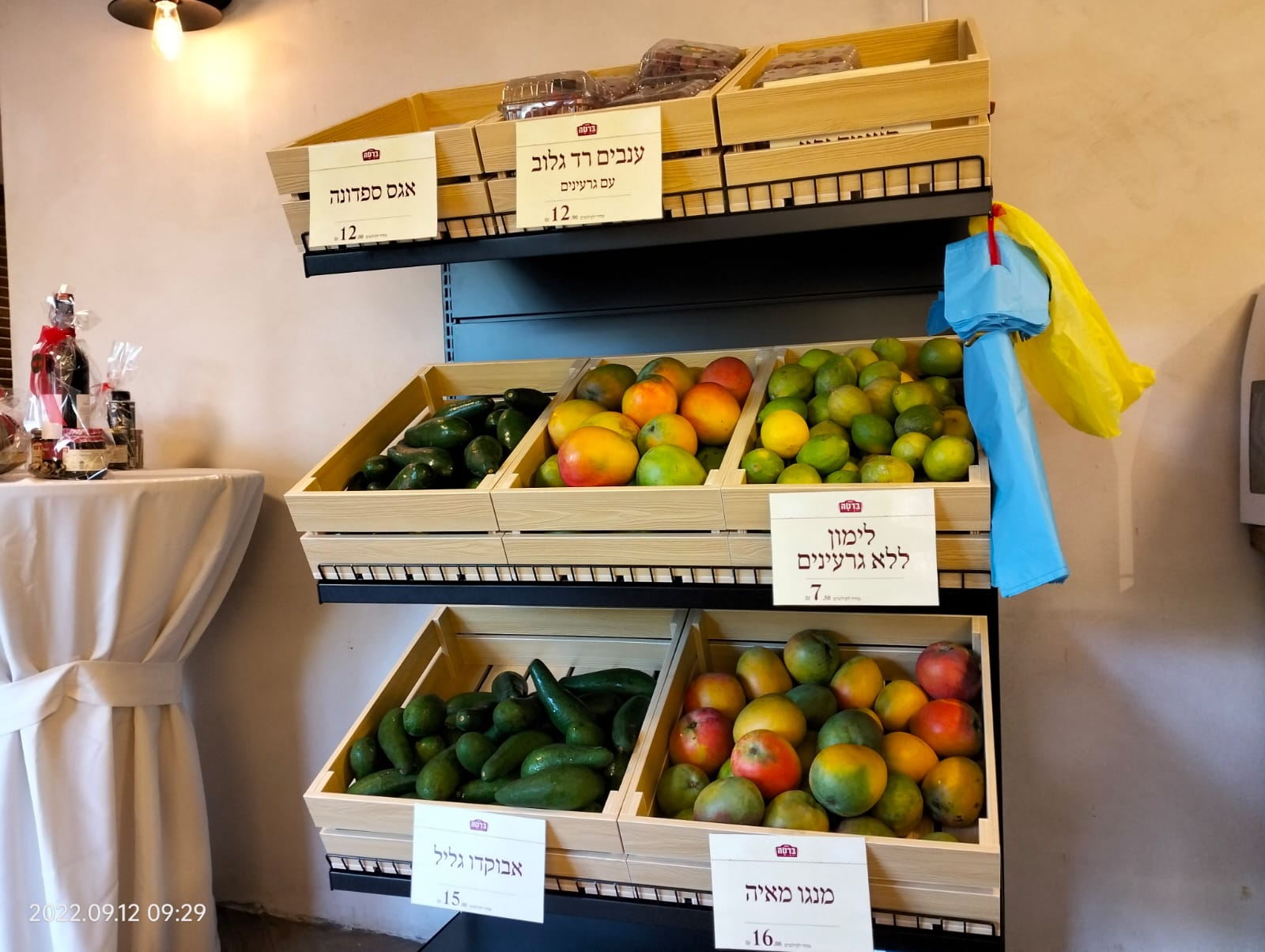 Wooden produce display with assorted fruits in trays, plus a blue bag hanging on the side.