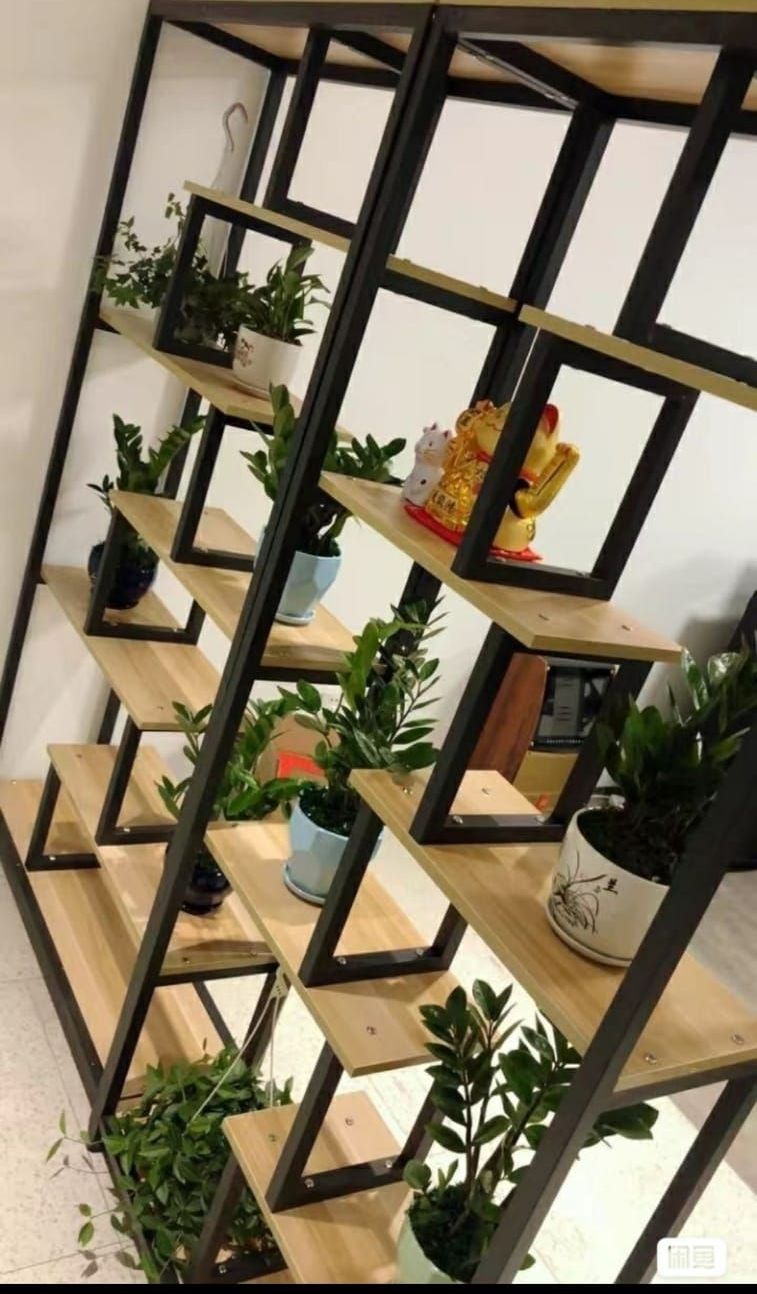 Black metal shelf with wooden platforms holding potted green plants and small decor pieces indoors