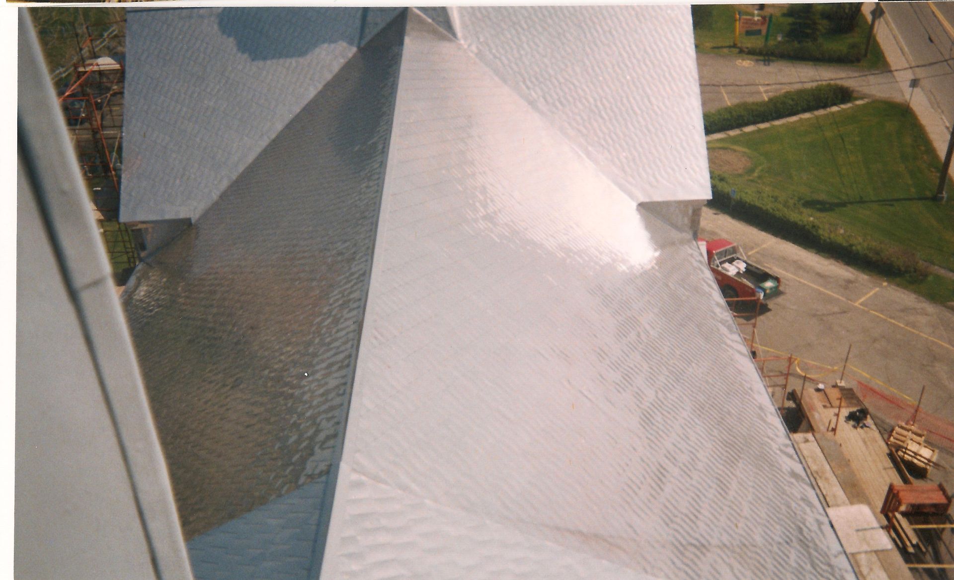 Vue d'en haut du toit brillant et argenté du bâtiment avec une voiture et de l'herbe verte.