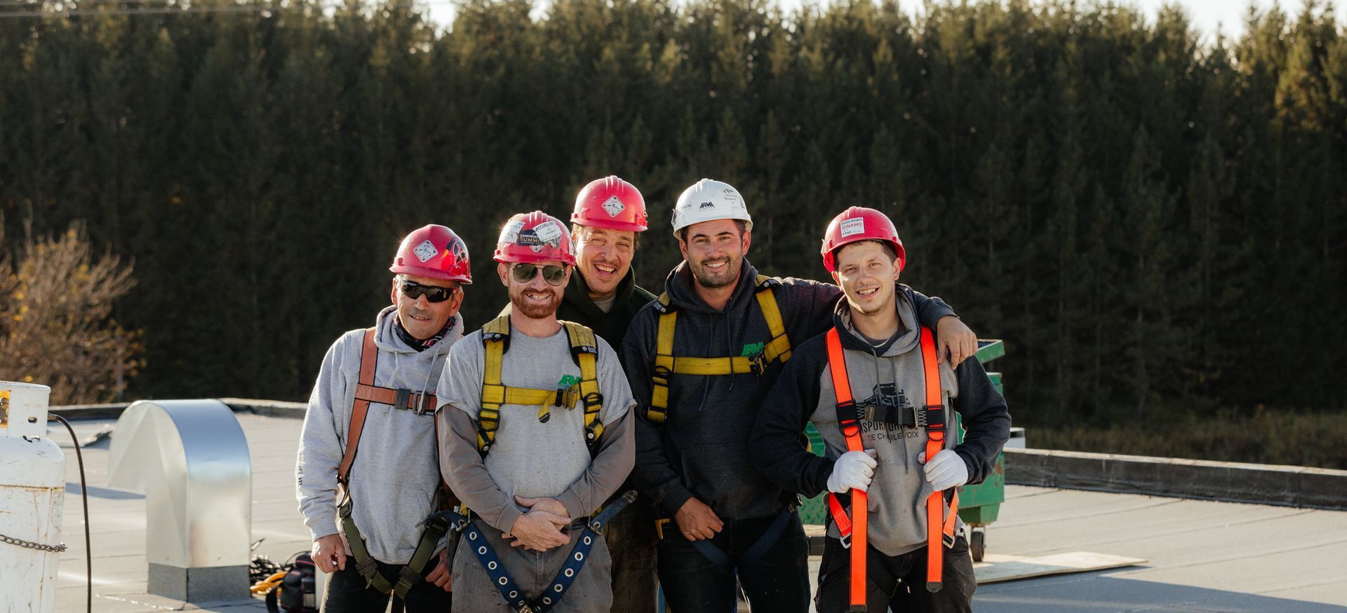 Cinq personnes, casquées et harnachées, posent pour une photo sur un toit. Une forêt sombre se dessine à l'arrière-plan.