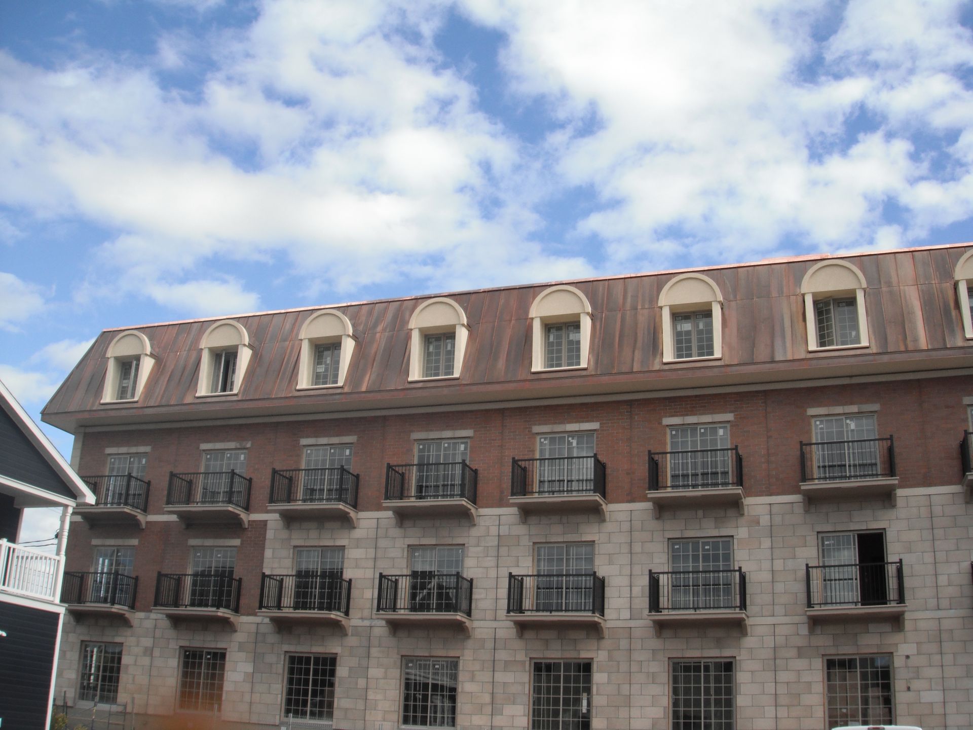 Bâtiment en pierre avec balcons et lucarnes sous un ciel nuageux