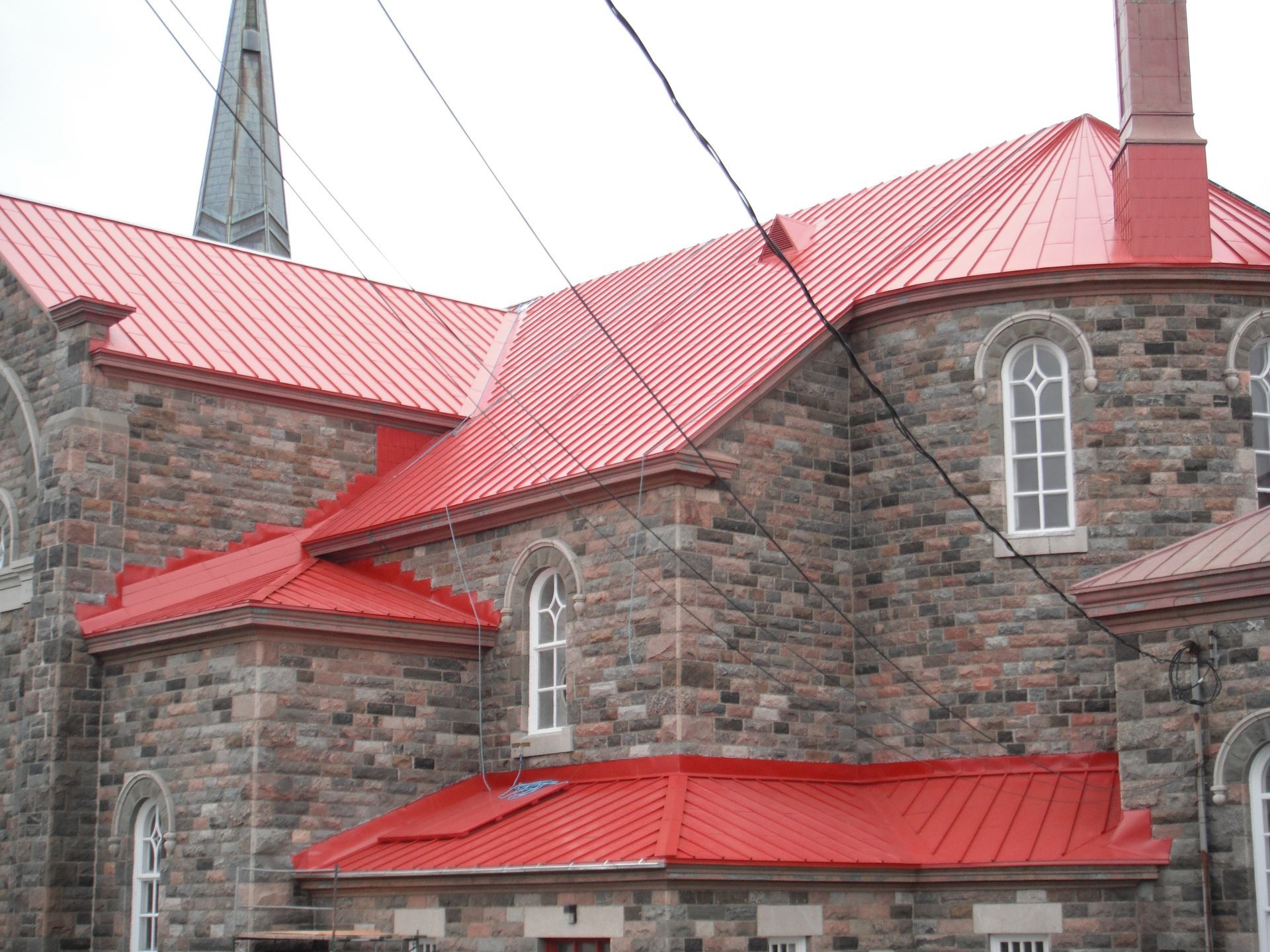 Église en pierre avec toit en tôle rouge et fenêtres cintrées